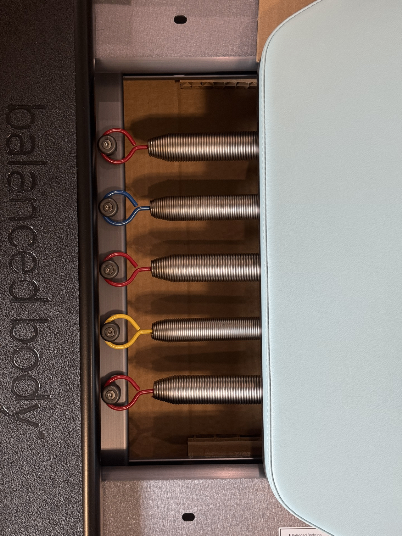 Close-up of a Pilates reformer's colorful springs and stainless carriage.